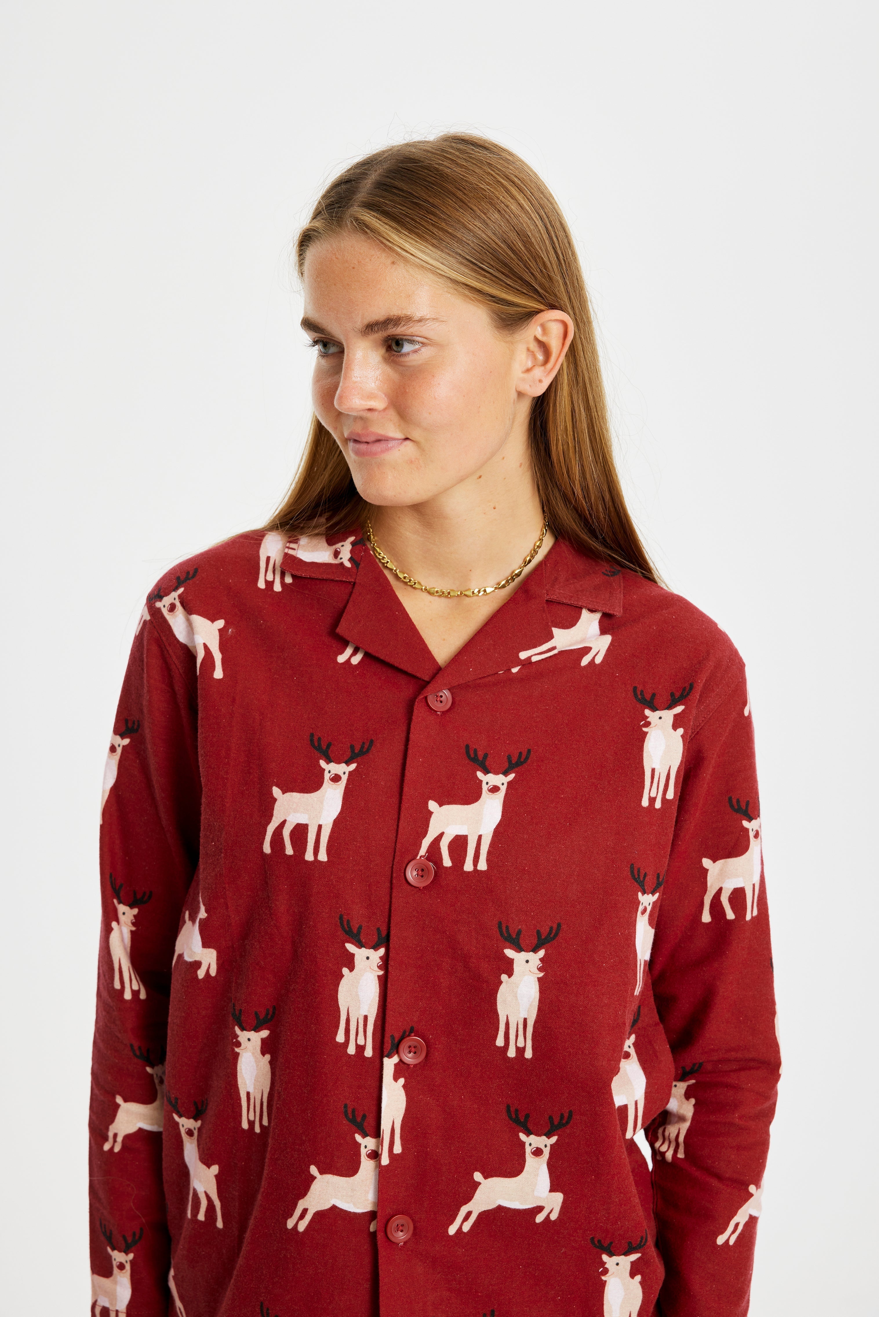 Een opzij kijkende vrouw in een rode kerstpyjama met rendieren erop.