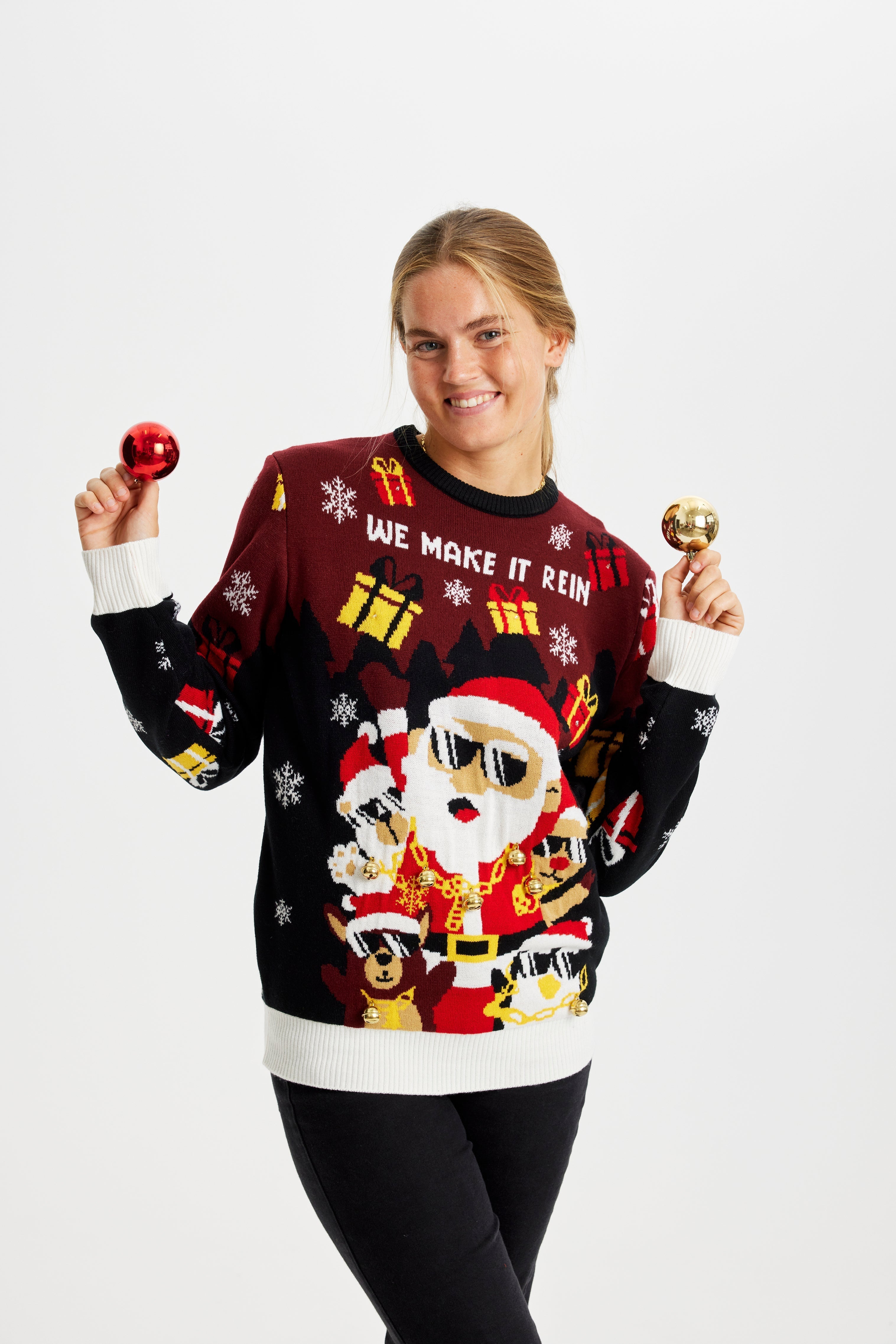 Een poserende vrouw die een rode en zwarte kersttrui draagt met een kerstfiguurtje en cadeautjes.