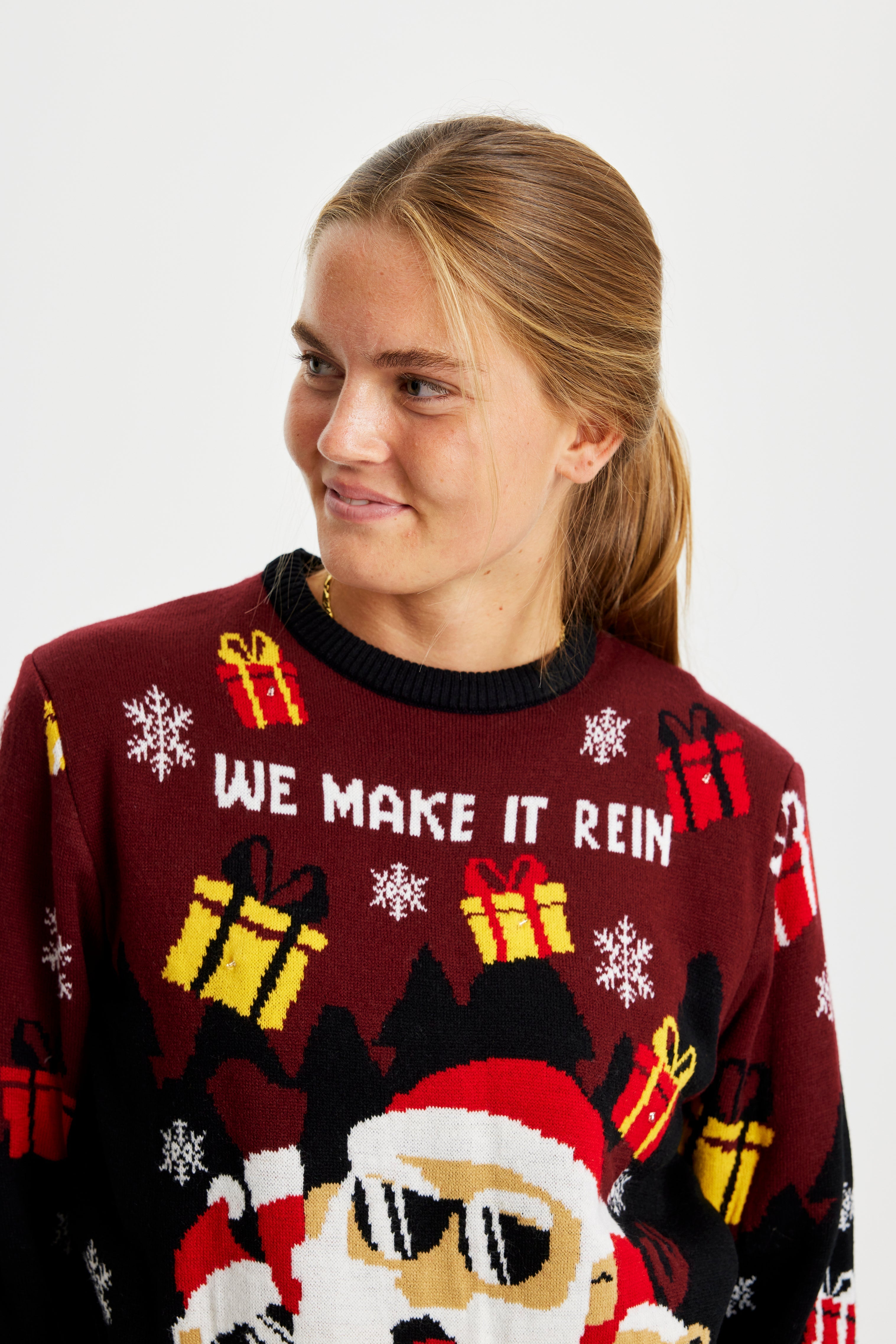 Een vrouw die opzij kijkt en een rode en zwarte kersttrui draagt met een kerstfiguurtje en cadeautjes.