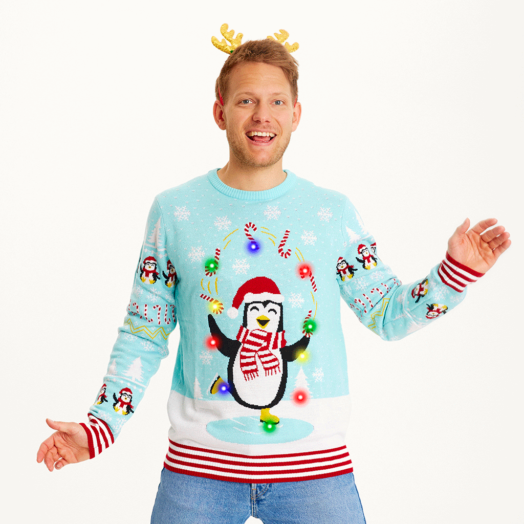 Een poserende man die een lichtblauwe kersttrui draagt met pinguïns en lichtjes.
