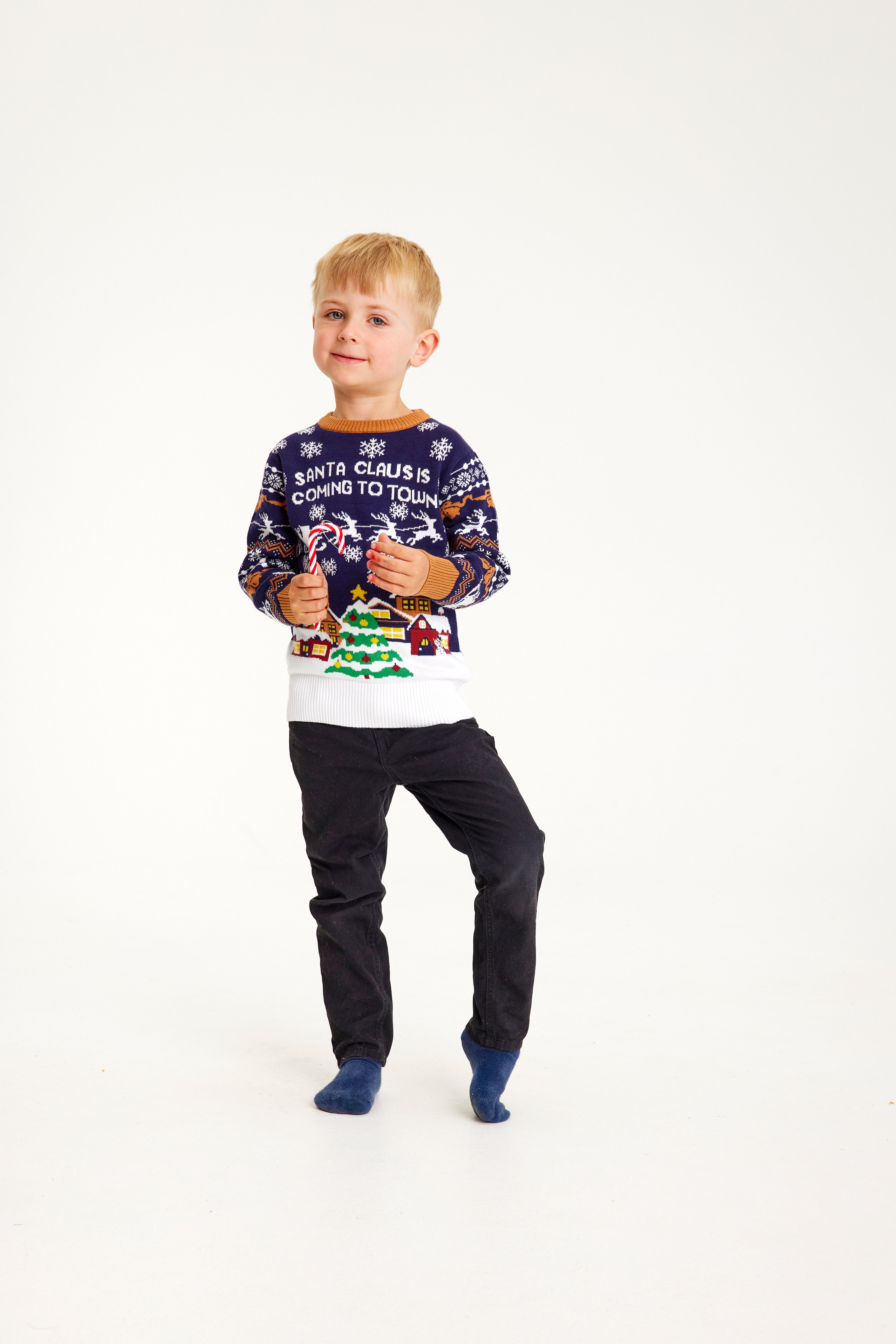 Een kind poseert terwijl het een blauwe kersttrui draagt met een besneeuwde stad.